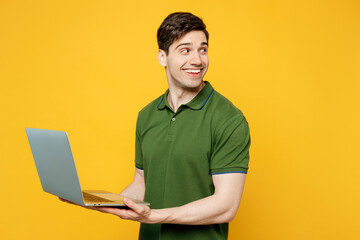 Side view young happy cheerful IT man wears green t-shirt casual clothes hold use work on laptop pc computer look aside on area isolated on plain yellow background studio portrait. Lifestyle concept.