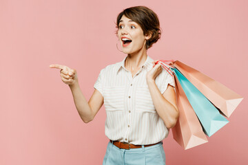 Side view young surprised woman wear casual clothes hold shopping paper package bags point finger on area isolated on plain light pastel pink color background studio Black Friday sale buy day concept