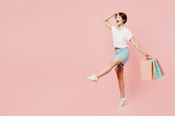 Fototapeta na wymiar Full body side view young woman wear casual clothes hold shopping paper package bags hold hand at forehead look far away distance isolated on plain pink background. Black Friday sale buy day concept.