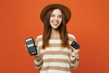 Young woman she wear striped sweater hat casual clothes hold wireless modern bank payment terminal to process acquire credit card isolated on plain orange red color wall background studio portrait. - obrazy, fototapety, plakaty