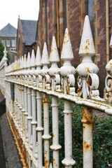 Vintage rusty iron fenceposts with spearpoint tops lined up in a row along a village street