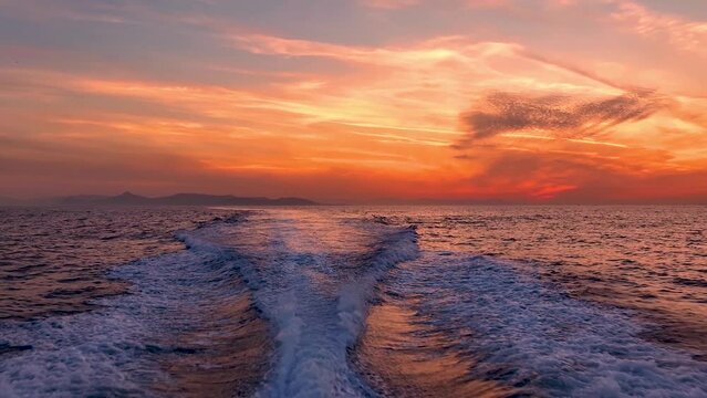 Beautiful view of a motor boat trail with waves and surf during a intense summer sunset over the ocean