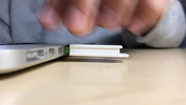 Male hand inserting USB memory storage into slot socket notebook on wooden desk close up view indoor. Transferring photo and date. Technology concept. 