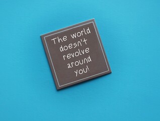 Brown card on blue background with handwritten text- The world doesn’t revolve around you - to remind we are the center of the universe, not as important that much, stop taking everything personally