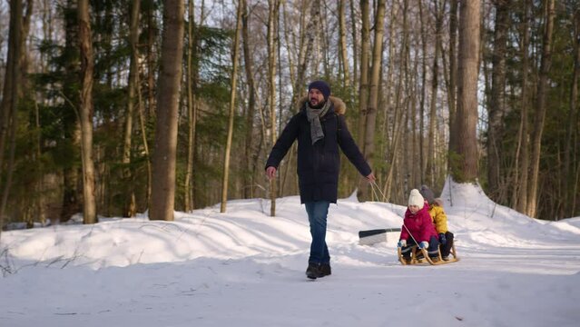 Father in warm clothes enjoys showing preschooler kids beauty of winter forest