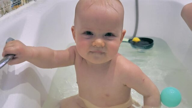 The cheerful child is having fun in the bathtub with some toys. Slow motion of a cute toddler boy enjoys his bath time.