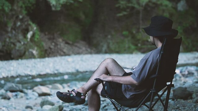 Handsome man camping relaxing on a riverbank no-face in the image of solo camping