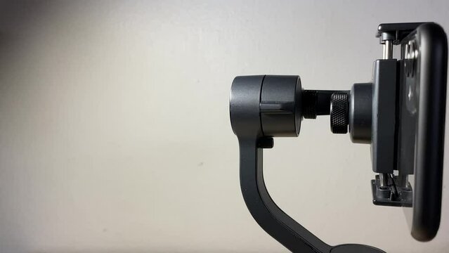 Black automatic gimbal stabilizer holding black phone on table against white wall indoor. with copy space. Technology and electronic gadget concept 