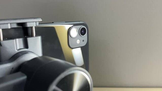 Black automatic gimbal stabilizer holding black phone with two lens on table against white wall indoor. Technology and electronic gadget concept 