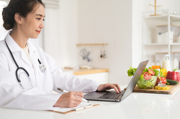 Close-up of dietitian hand writing with laptop giving online weight loss and healthy diet...