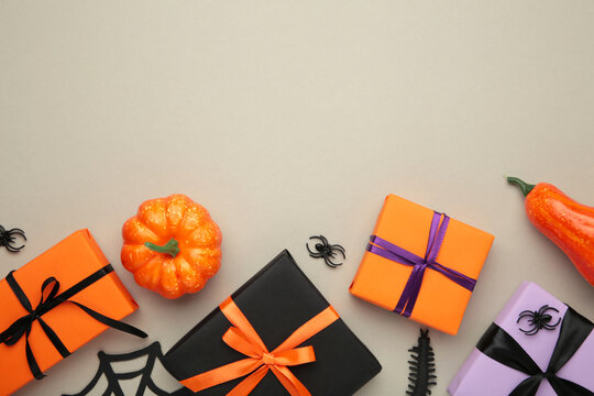 Happy Halloween holiday concept. Flat lay gift boxes, orange pumpkins, bats, spiders on grey background. Halloween greeting card template.
