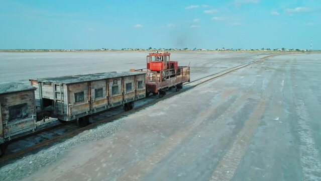 Aerial over railway carriages driving at salty lake shore. Salt mining in Altai region of Russia