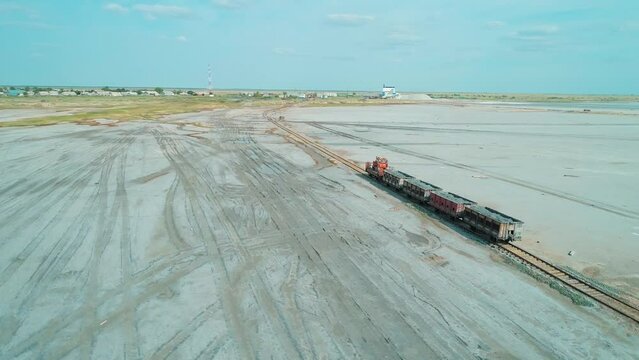 Aerial over railway carriages driving at salty lake shore. Salt mining in Altai region of Russia