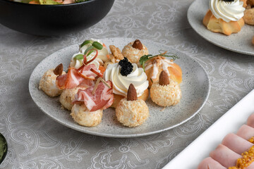 Holiday savory profiteroles with caviar, cream cheese and dill on a white plate on a white background. A plate on a festive table.