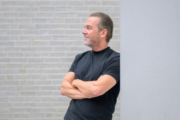 Man leaning against a wall with his arms crossed and looking expectantly