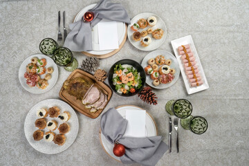 Fototapeta na wymiar Different traditional food for the New Year's table, decorated with balls and fir cones. Russian salad, pastries, appetizers and boiled pork.