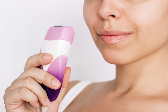 Cropped shot of young caucasian woman holding epilator in her hand for getting rid of unwanted hair on a white background. Hair removal