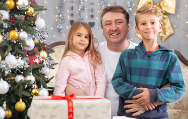 Fototapeta na wymiar Happy father with his son and daughter near the Christmas tree in the living room