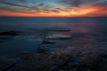 Long exposure of sea waves over flat rocks at the sunset. - 648911033