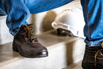 Male feet wearing leather safety shoes with white protective helmet or hard hat on concrete stair...