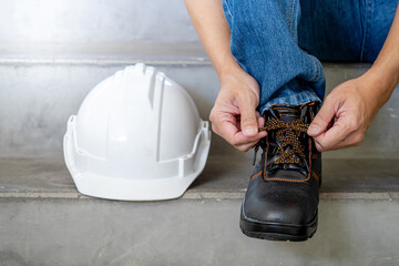 Male worker hands tying shoelaces on leather safety shoes with white protective helmet or hard hat...