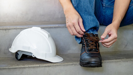 Male worker hands tying shoelaces on leather safety shoes with white protective helmet or hard hat...