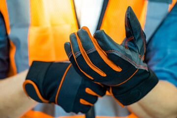Male construction worker with reflective orange vest putting black protective gloves on his hands....
