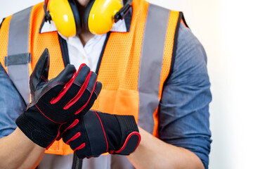 Male construction worker with reflective orange vest and yellow ear muffs putting black and red...