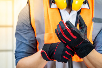 Male construction worker with reflective orange vest and yellow ear muffs putting black and red...