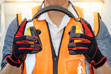 Male worker with reflective orange vest and protective hand gloves pulling yellow safety ear muffs...