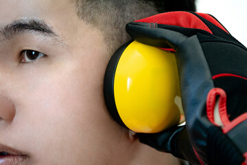 Asian male worker with black and red protective hand gloves holding yellow safety ear muffs or ear...