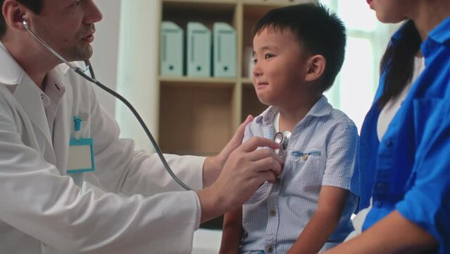Small cheerful boy looking at doctor listening to his chest with stethoscope during visit