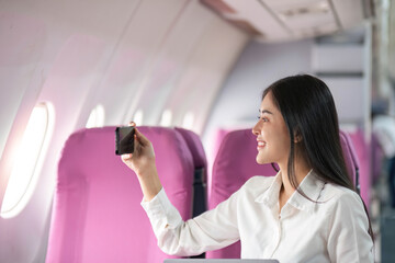 Smiling tourist woman taking a selfie on her mobile phone waiting on the plane. Passengers traveling abroad during the weekend air flight concept
