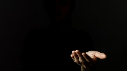 A woman's hand is in the darkness, making a gesture with her hand as if she is holding something.