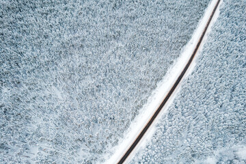 top view of a black strip of road among trees in the snow