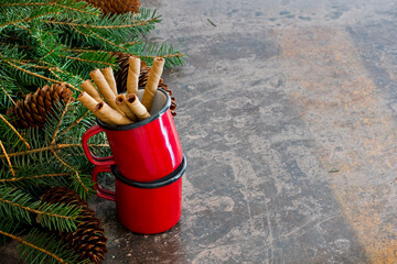 Fondo navideño con piñas y ramas de abeto junto a tazas rojas con barquillos de chocolate