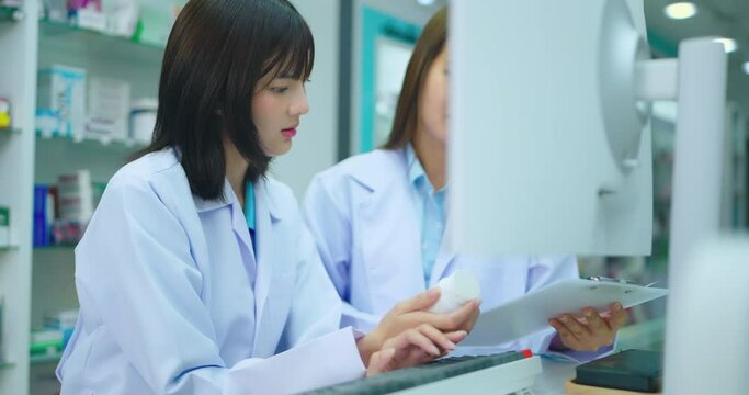 Young asian female pharmacist using computer in pharmacy shop. She research drug information at pharmacy shop.