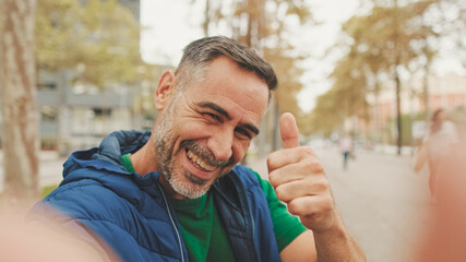 Mature man wearing casual clothes, sitting on bench in the park, talking on video call from smartphone