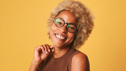 Close up, happy friendly girl in glasses, wearing brown top playfully flirting smiling looking at camera isolated on orange background, studio shot