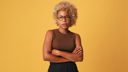 Irritated girl in glasses, wearing brown top listens attentively to someone, sighs, is bored and tired of empty promises isolated on orange background