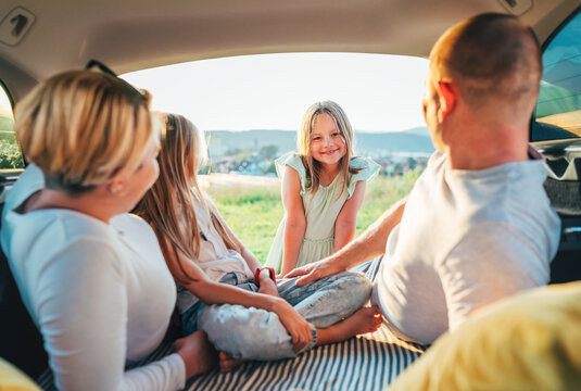  Portrait of happy smiling little girl gazing at camera. Happy young couple with two daughters inside the car trunk during auto trop. They laughing and chatting. Family values, traveling concept