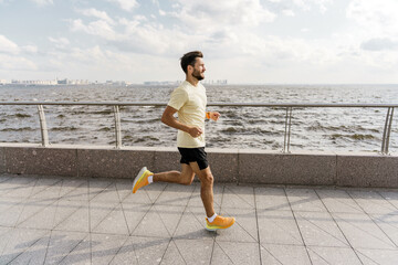 Motivation and an active lifestyle in the city. The trainer is a strong man fitness in comfortable outdoor sportswear. Runner active interval training and warm-up. - obrazy, fototapety, plakaty