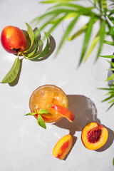 Refreshing peach tea with ice and mint. Homemade cold healthy drink on a light background with fresh fruits, palm leaf and shadows.