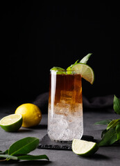 Coffee brew with tonic, ice and lime in a tall glass on a dark background with citrus fruit and...
