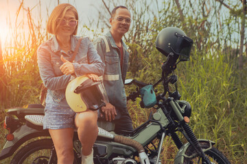 asian couples standing beside enduro motorcycle with high green grass background