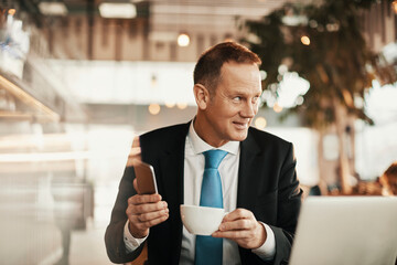 Middle aged businessman using a smartphone while having coffee in a cafe decorated for christmas and the new year holidays