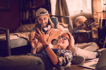 Young couple using a smartphone while playing the guitar in the bedroom at home