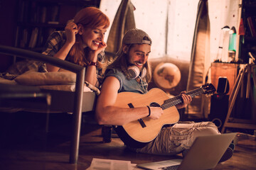 Young couple playing the guitar and singing together in the bedroom at home