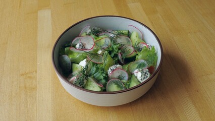 Ready dish with radish and cucumber lettuce, salad in a plate on the table, close-up