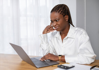 Unhappy young black woman employee using laptop at office